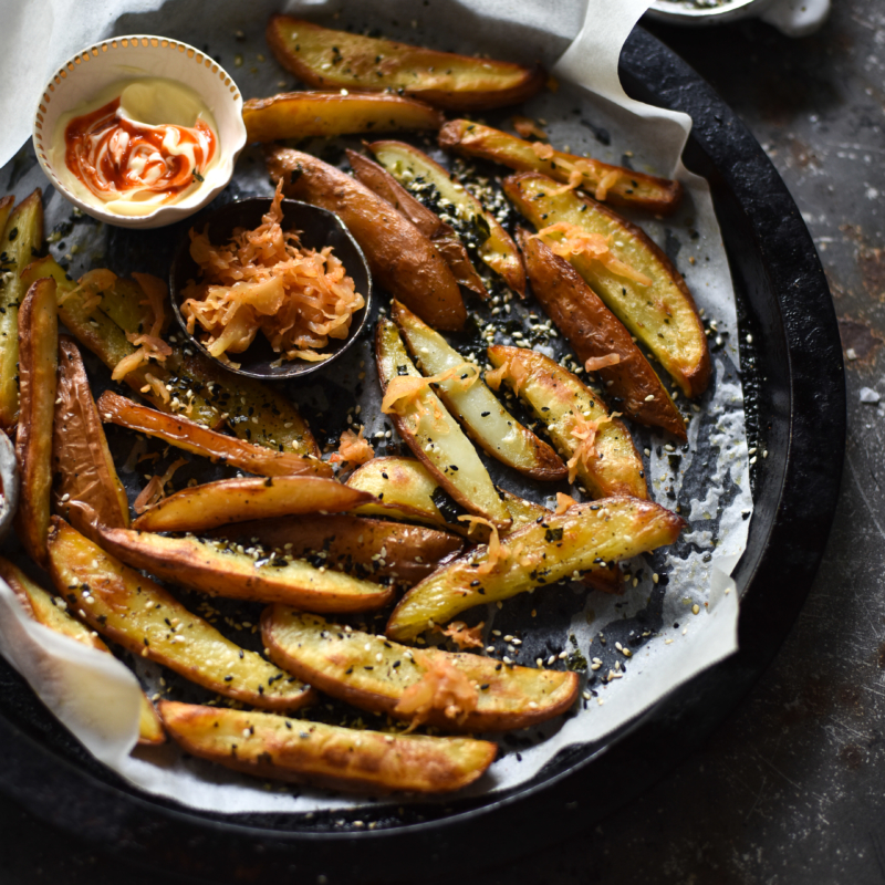 An aerial image of vegan furikake fries on a lined baking dish atop a wooden table.