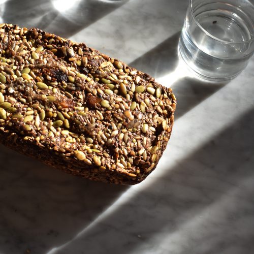 Nut free Life Changing Fruit Loaf on a white marble table surrounded by glasses of water.