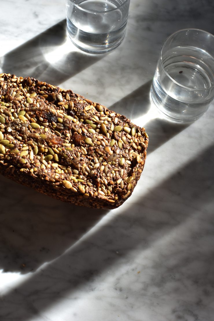 Nut free Life Changing Fruit Loaf on a white marble table surrounded by glasses of water.