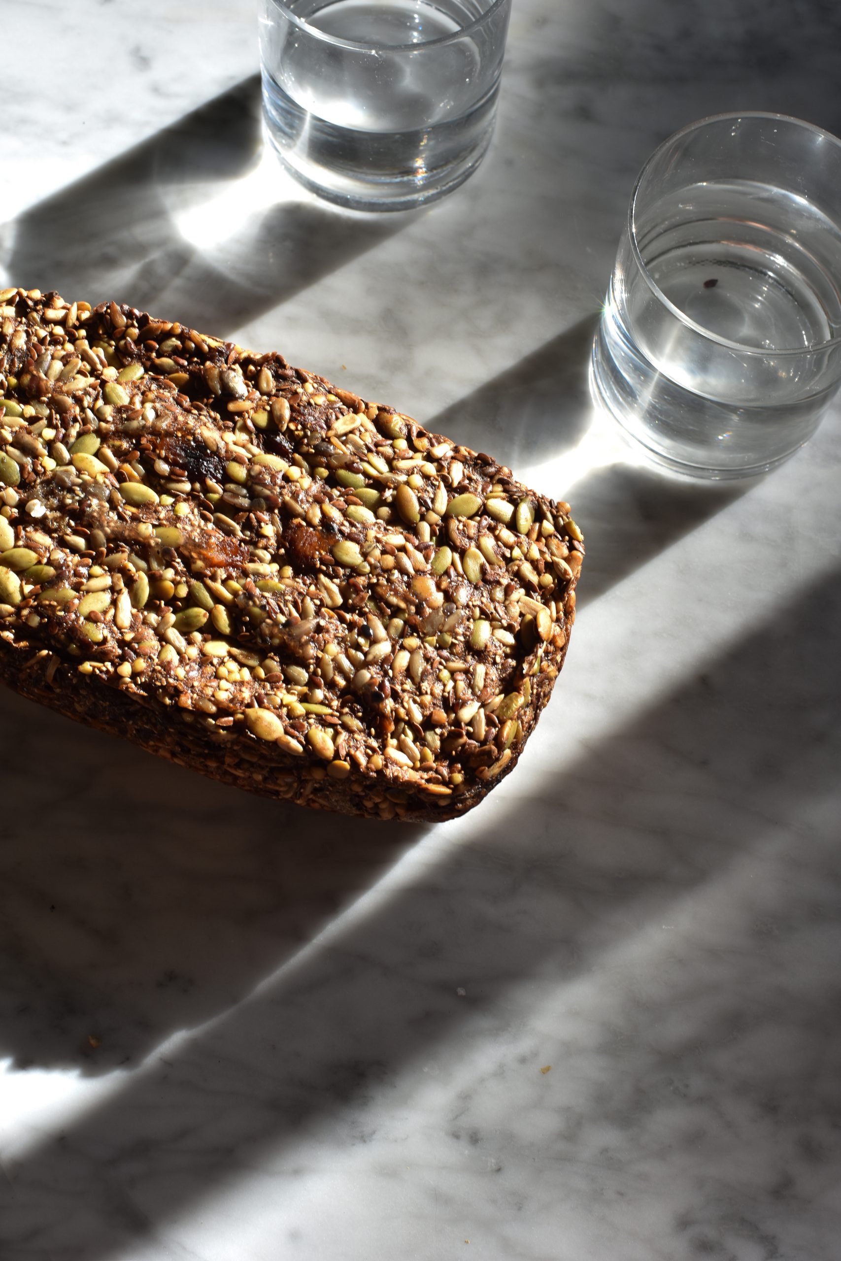 Nut free Life Changing Fruit Loaf on a white marble table surrounded by glasses of water.