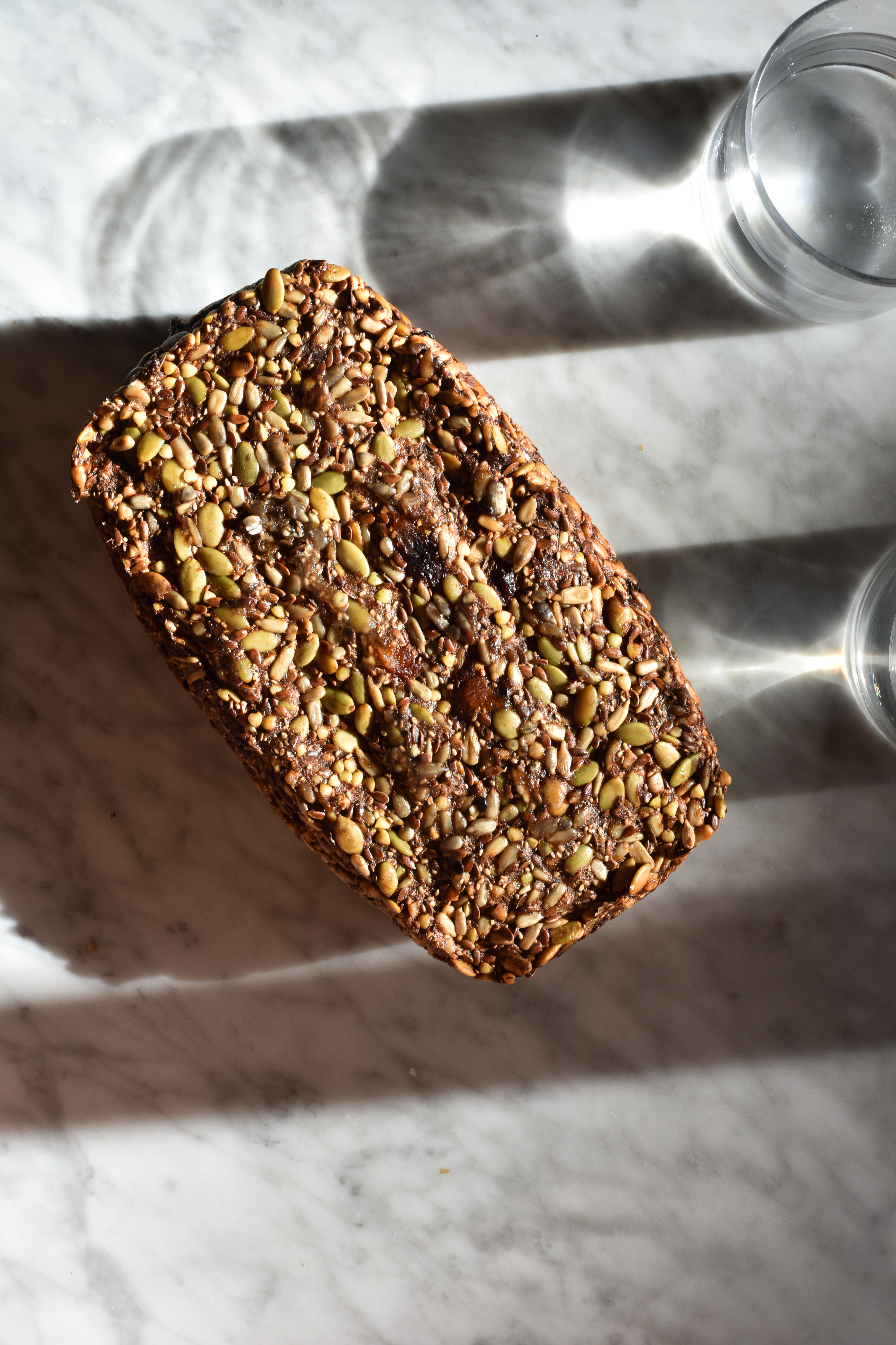 Nut-free gluten-free Fruit Loaf on a marble backdrop with sunlit water glasses