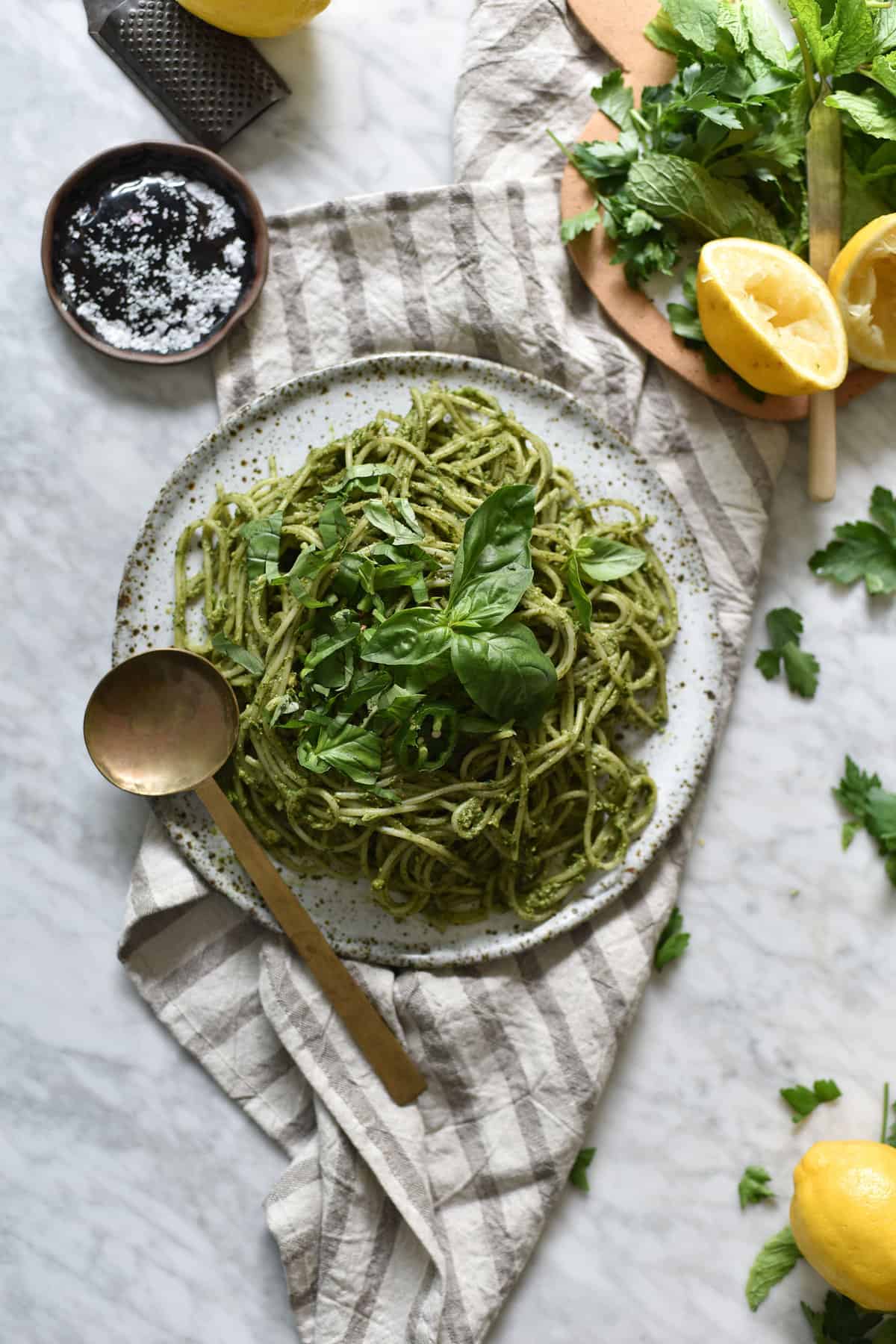Gluten free and vegan avocado and herb sauced pasta on a white ceramic plate atop a white marble table. 