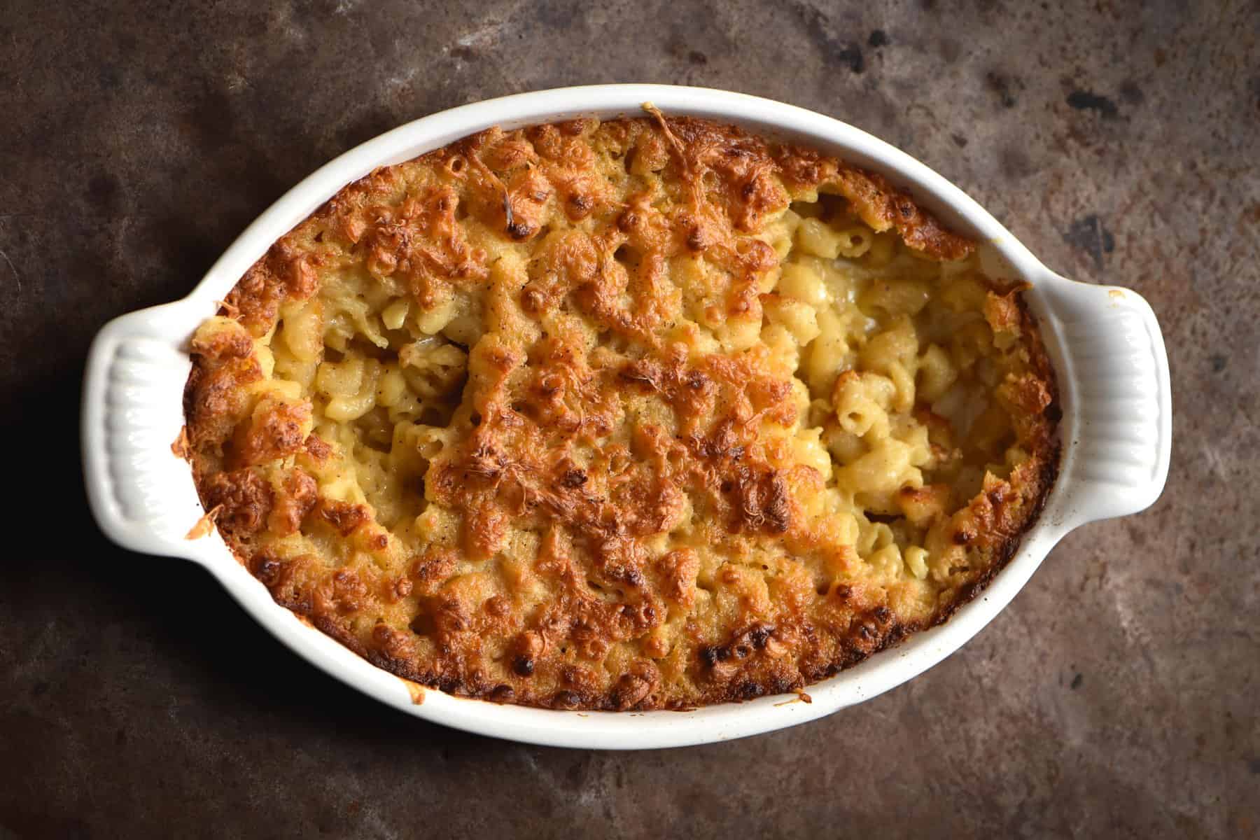 A close up of a vegan, gluten free and FODMAP friendly mac and cheese bake against a rusty backdrop
