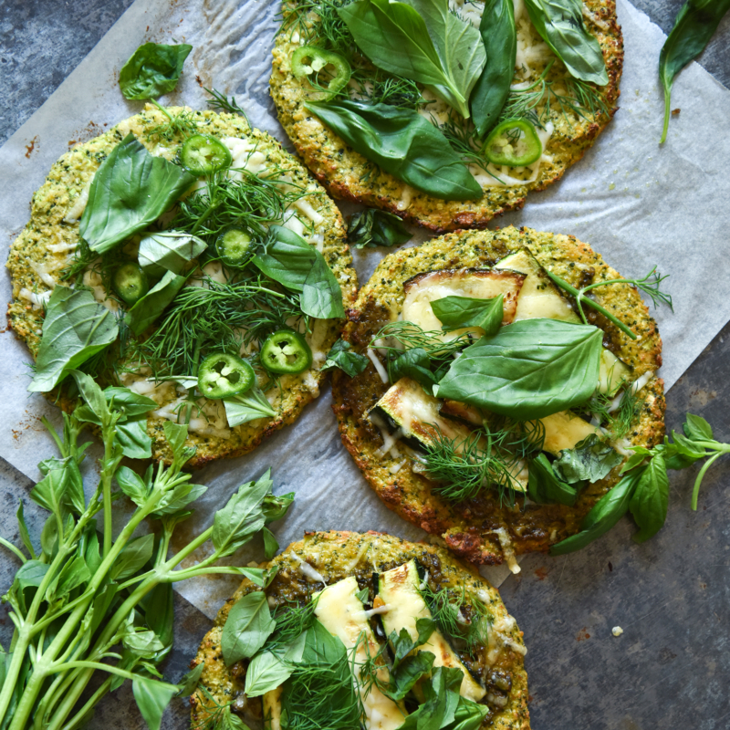 An aerial view of gluten free broccoli pizza bases on a medium blue steel pizza tray