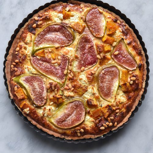 Gluten free fig, pumpkin, pine nut and goats cheese tart on a light marble backdrop