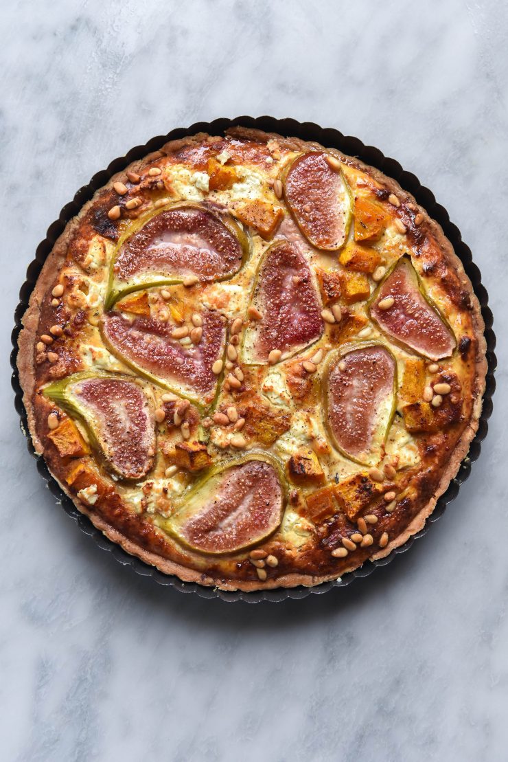 Gluten free fig, pumpkin, pine nut and goats cheese tart on a light marble backdrop