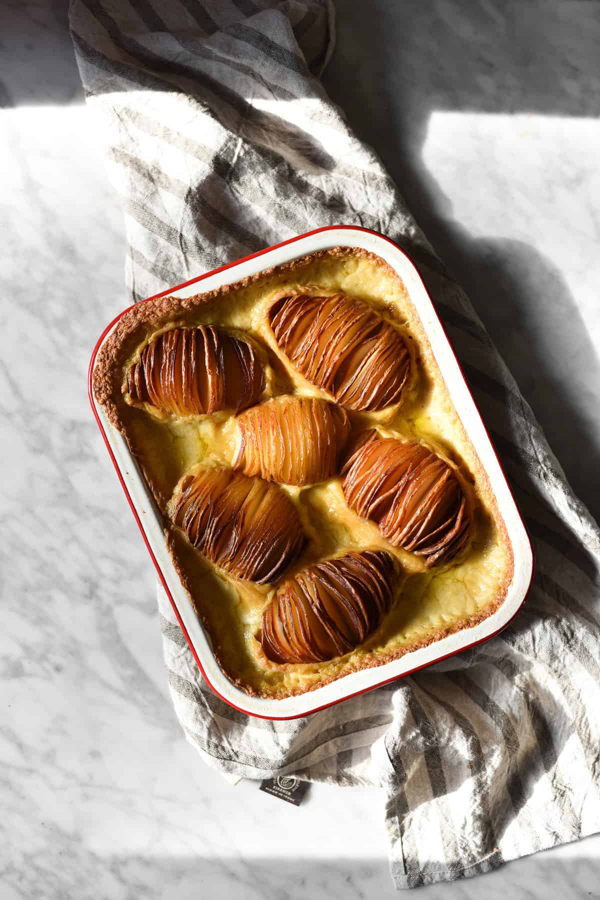 Gluten free, vegan, FODMAP friendly cheesy hasselback potato bake on a sunny marble backdrop