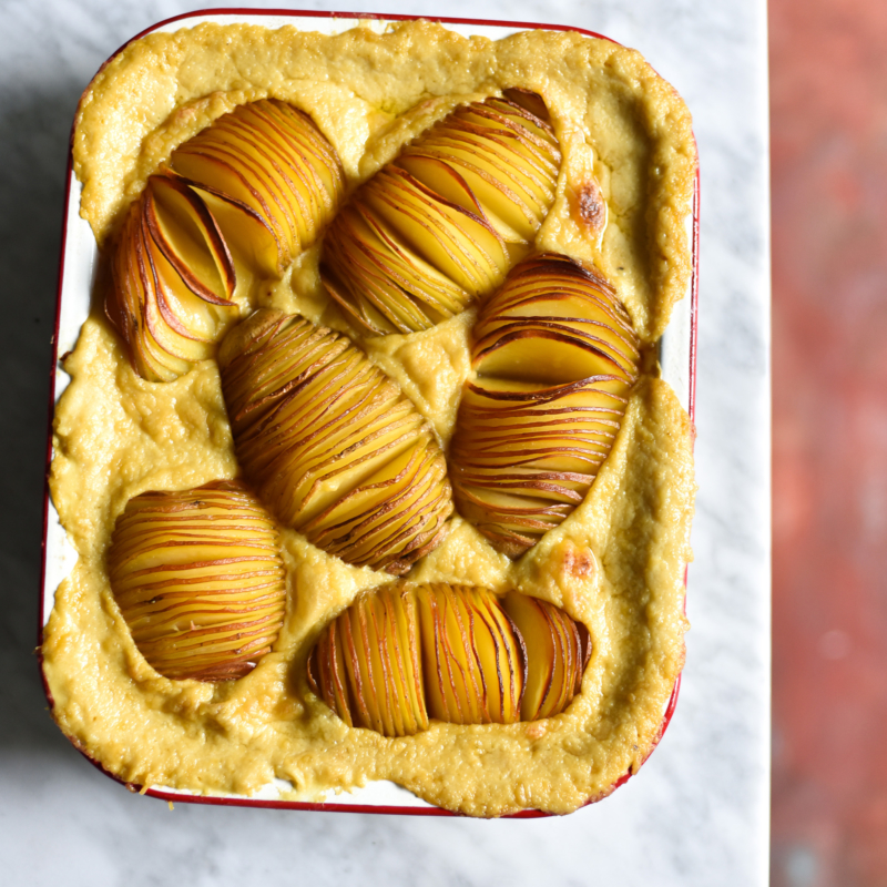 Gluten free, vegan, FODMAP friendly cheesy hasselback potato bake in a white baking dish atop a white marble table