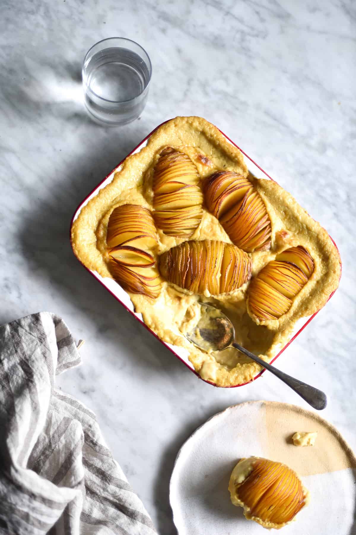 Gluten free, vegan, FODMAP friendly cheesy hasselback potato bake in a white baking dish atop a white marble table