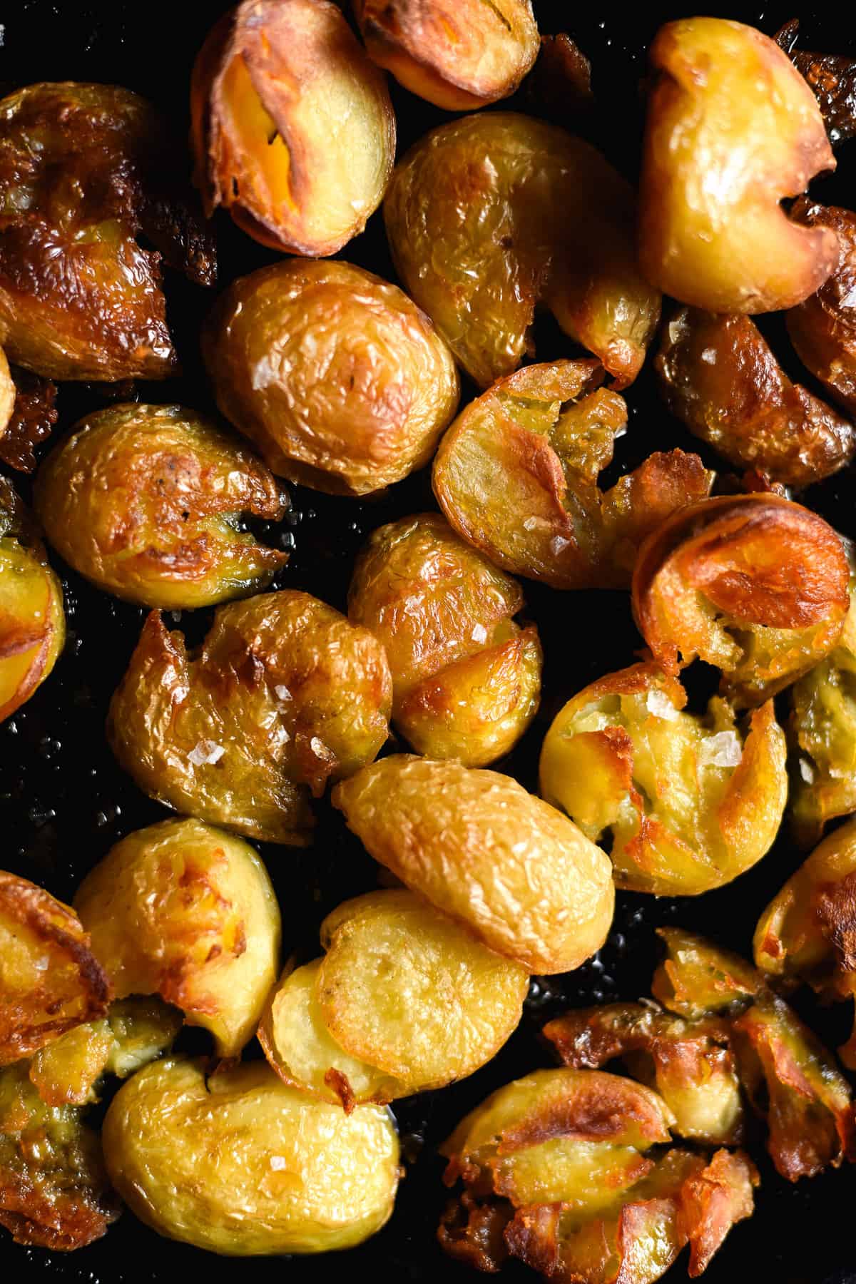 An aerial close up image of crispy salt and vinegar potatoes on a black baking tray.