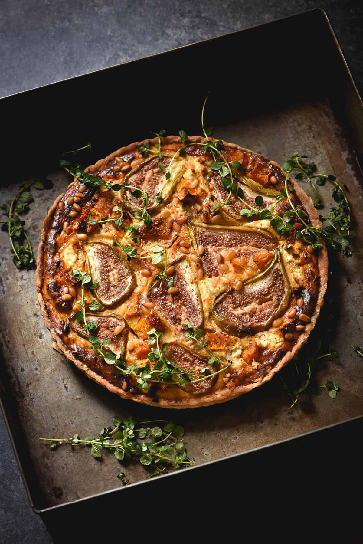 Gluten free savoury fig tart with roasted pumpkin, thyme, goats cheese and pine nuts on a dark blue backdrop