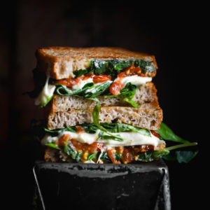 A moody side on image of a gluten free caprese toastie on a black baking tin against a black backdrop