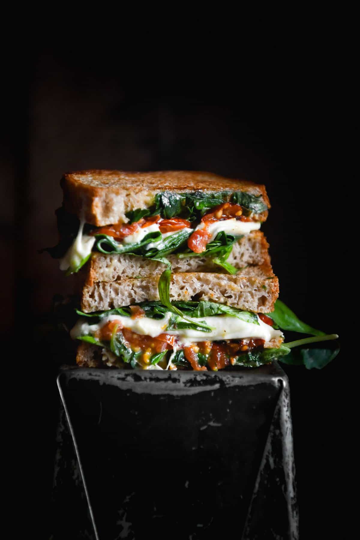 A side on moody image of a gluten free sandwich bread toastie atop a black metal tin against a black backdrop. 