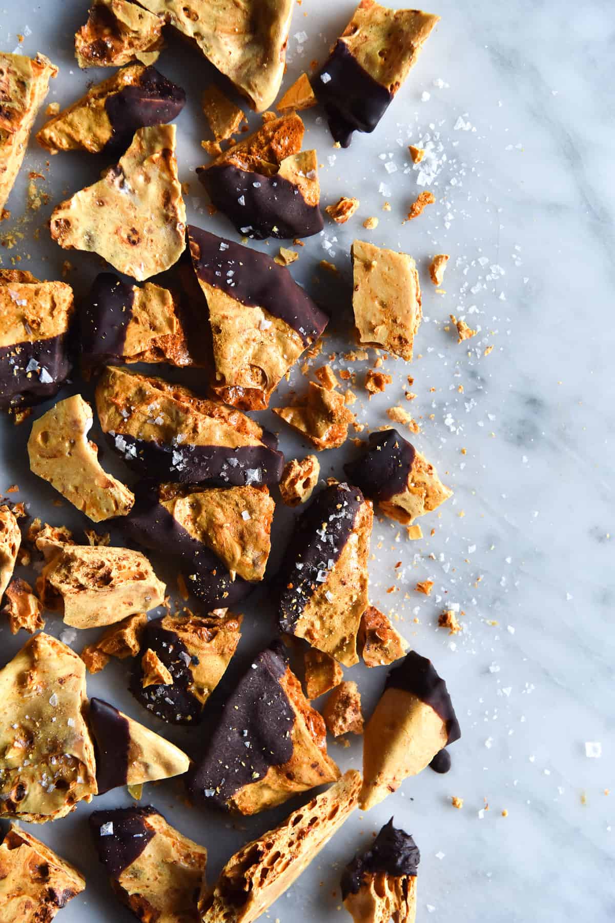 An aerial image of vegan honeycomb shard dipped in chocolate on a white marble table