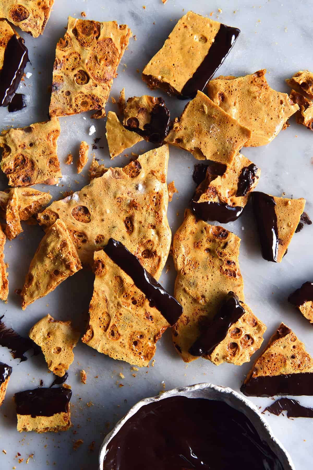 An aerial image of vegan honeycomb shard dipped in chocolate on a white marble table