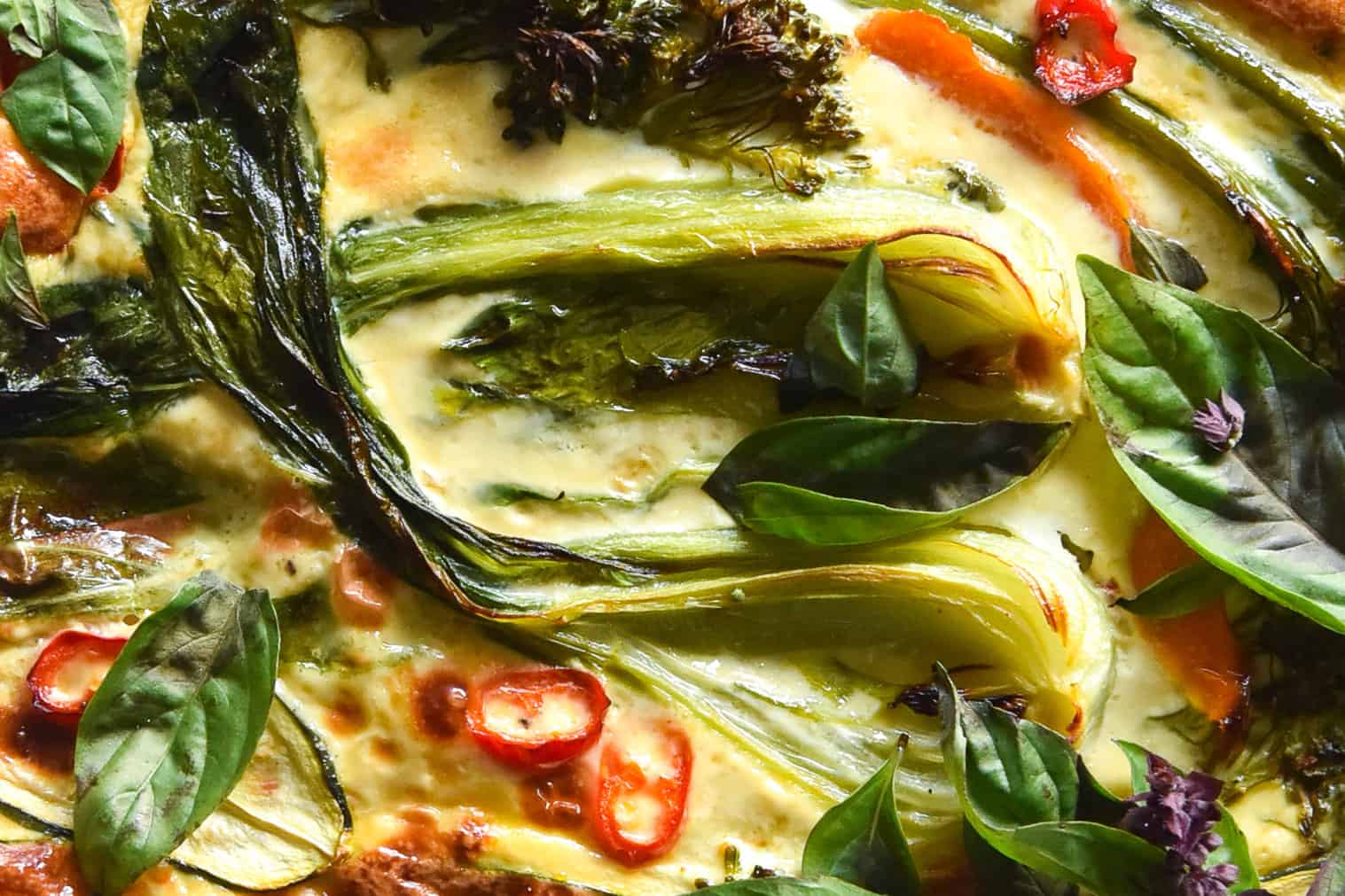 An aerial macro close up of a Thai green curry frittata filled with pak choi, chilli and other vegetables and topped with chilli and Thai basil.