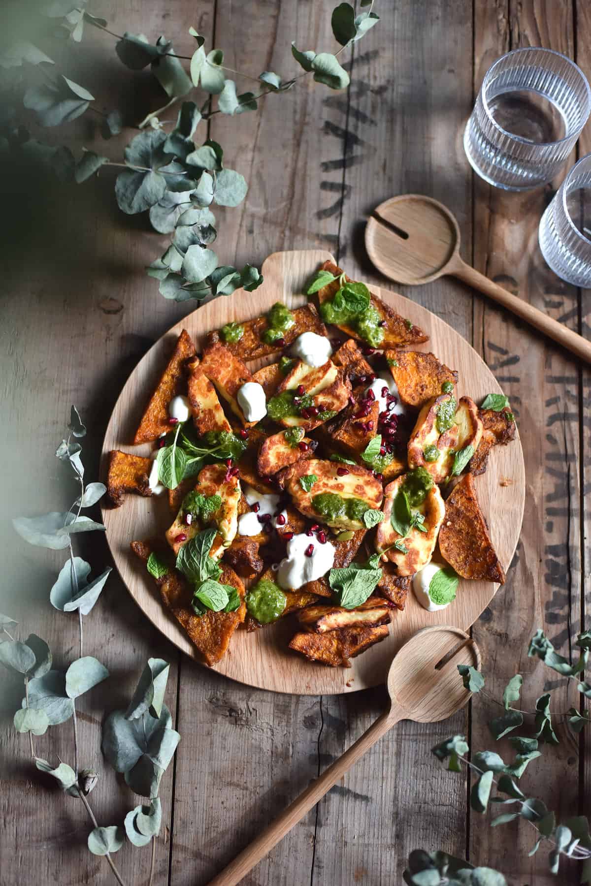 Spice roasted pumpkin haloumi salad with yoghurt, pomegranate and a herb and preserved lemon dressing on a wooden table surrounded by greenery.