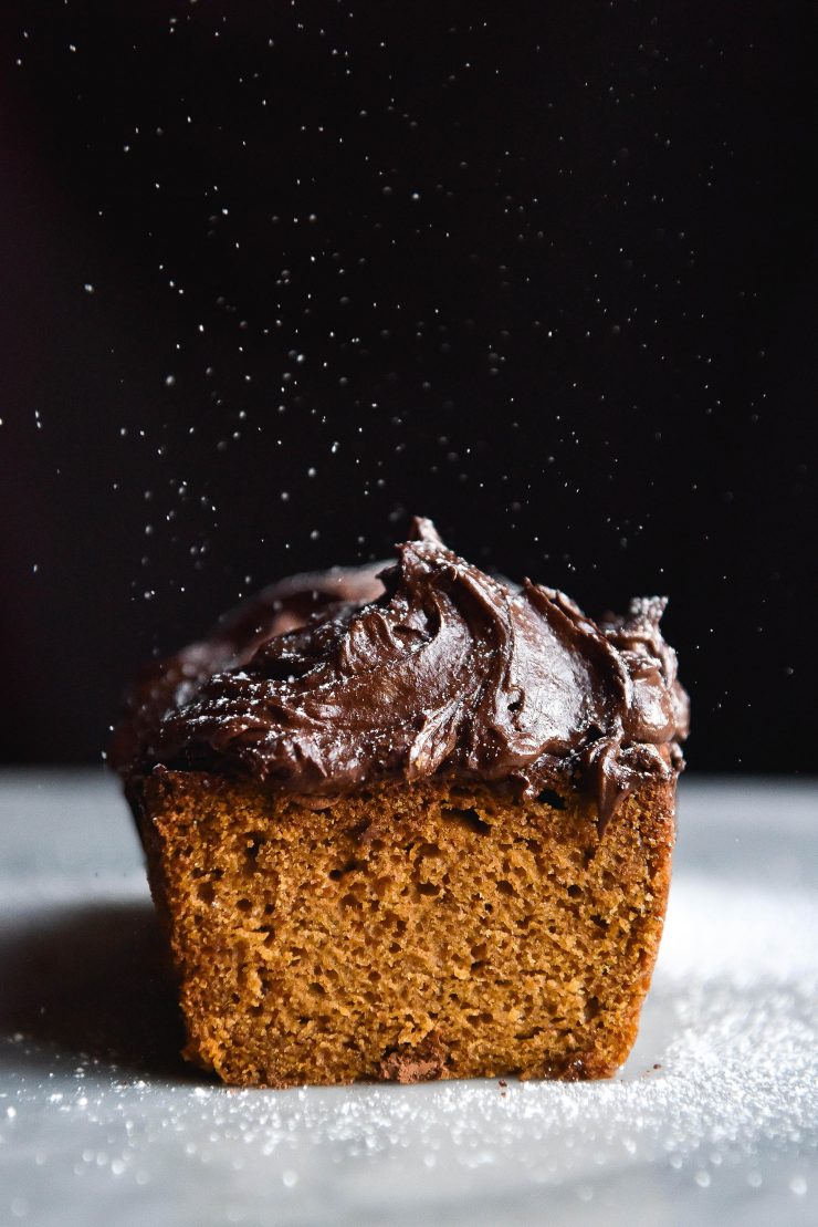 Front on view of gluten free pumpkin loaf with a heaping of chocolate buttercream and a sprinkle of icing sugar