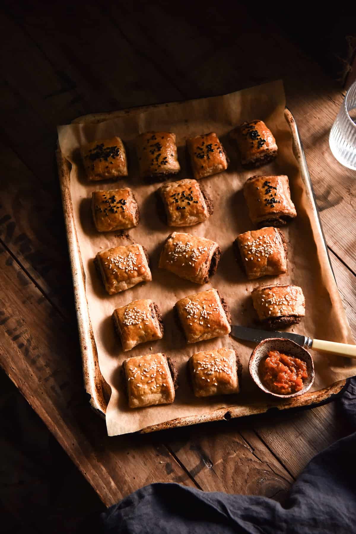A moody aerial image of vegetarian sausage rolls on a baking tray atop a dark and moody wooden table.