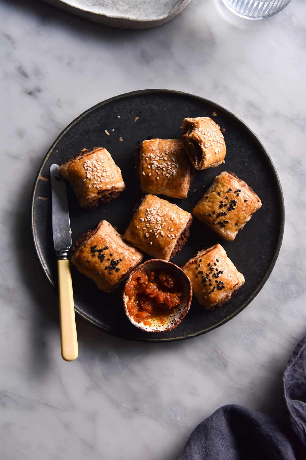 An aerial image of vegetarian gluten free sausage rolls on a dark ceramic plate atop a white marble table.