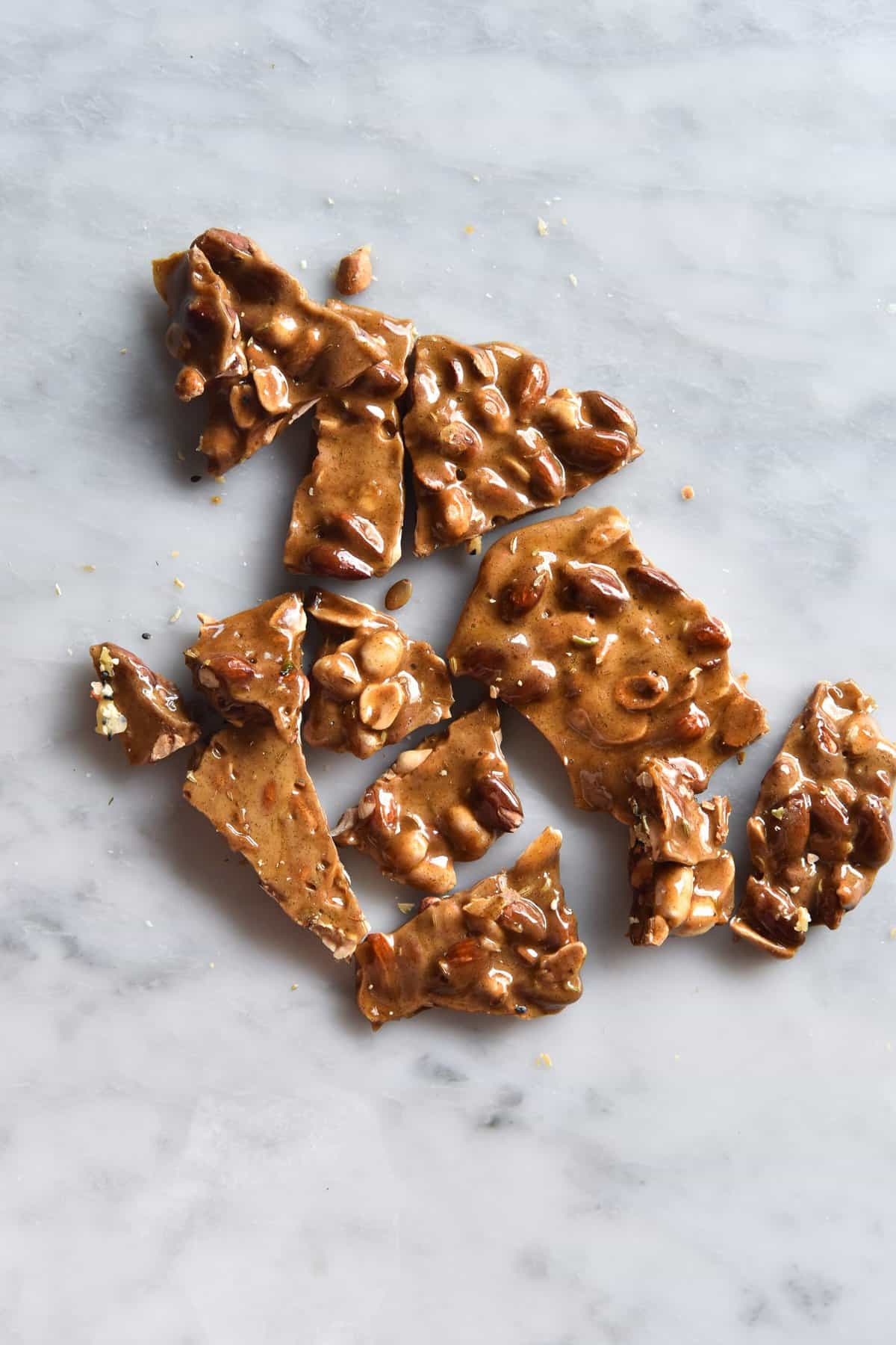Brown butter nut brittle without corn syrup snapped into pieces atop a white marble table