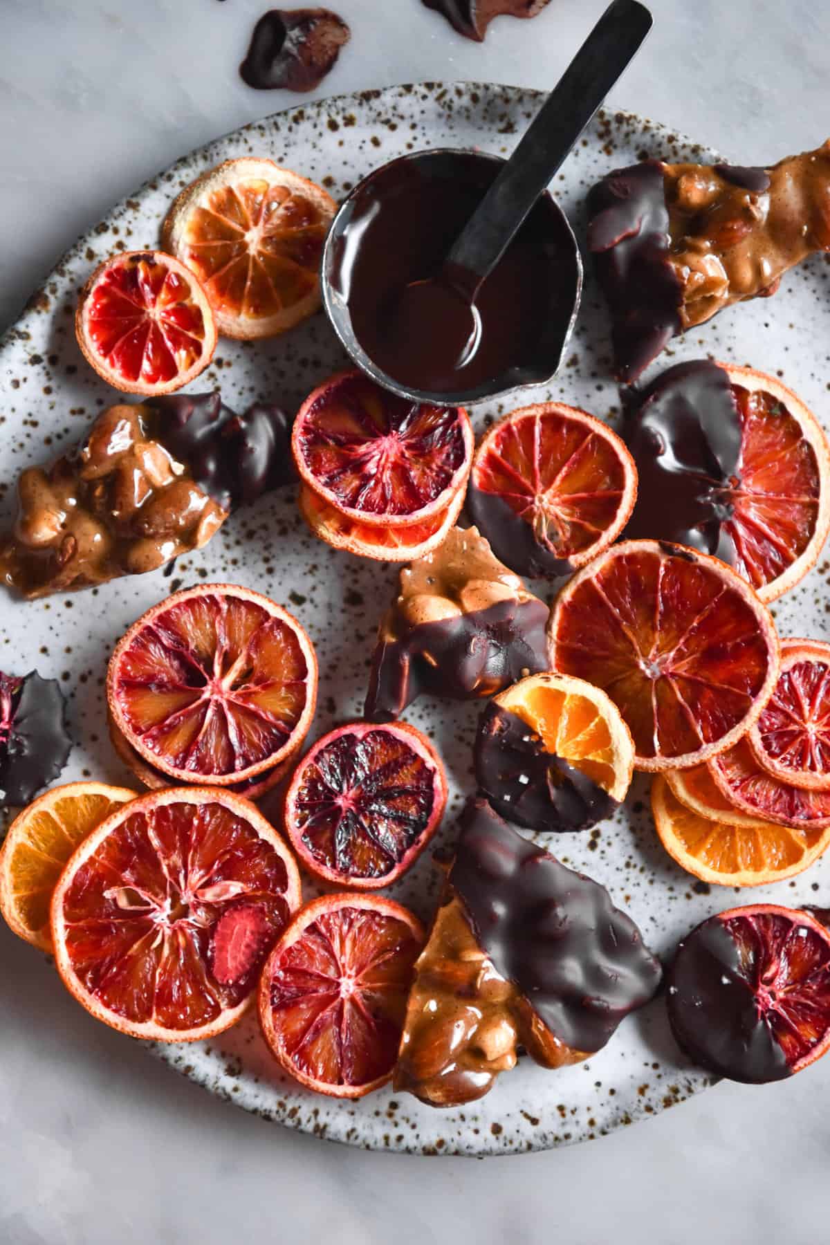 An aerial image of freeze dried blood oranges dipped in vegan chocolate on a sunlit white marble table. 