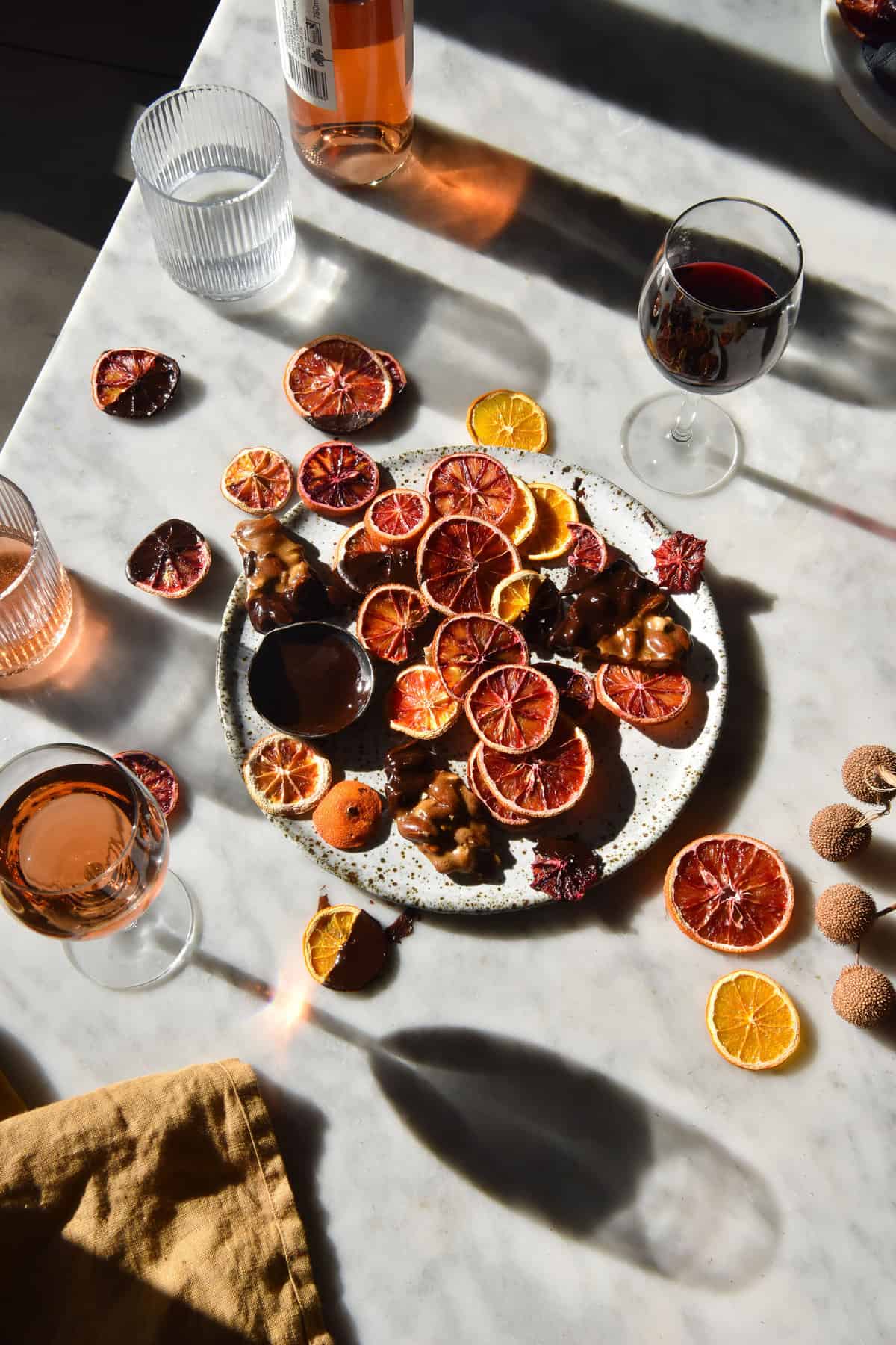 An aerial image of freeze dried blood oranges dipped in vegan chocolate on a sunlit white marble table. 