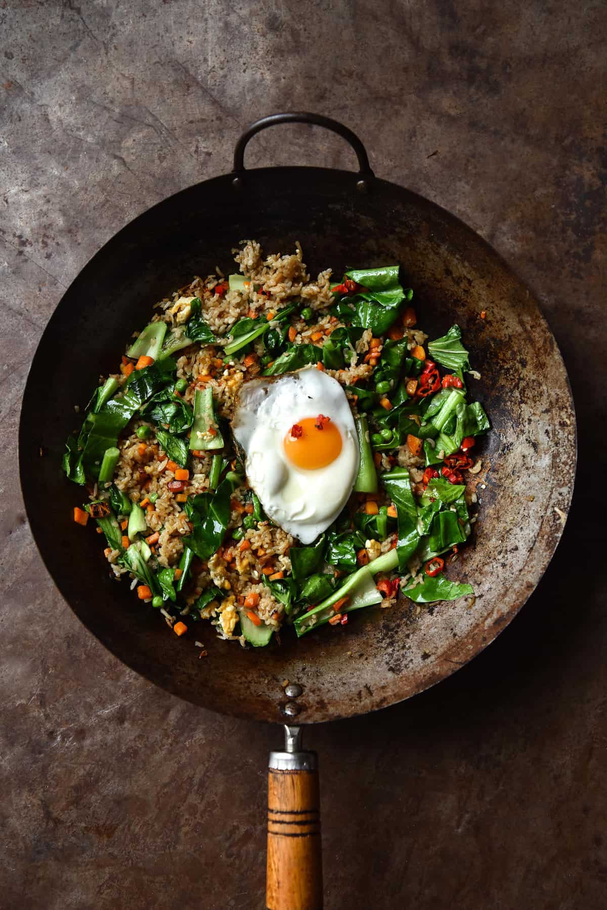 An aerial image of a dark rusty wok filled with low FODMAP fried rice atop a dark rusty backdrop