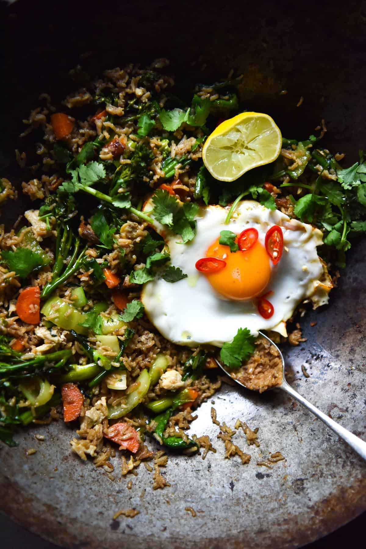 An aerial close up image of a wok filled with vegetarian fried rice and topped with a fried egg.