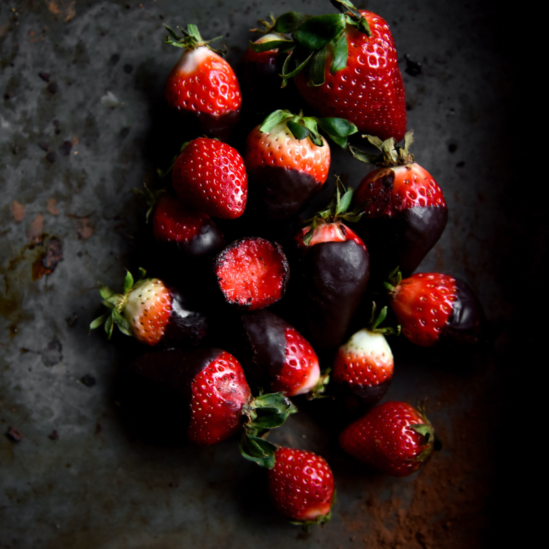 An aerial moody image of vegan chocolate covered strawberries on a dark backdrop
