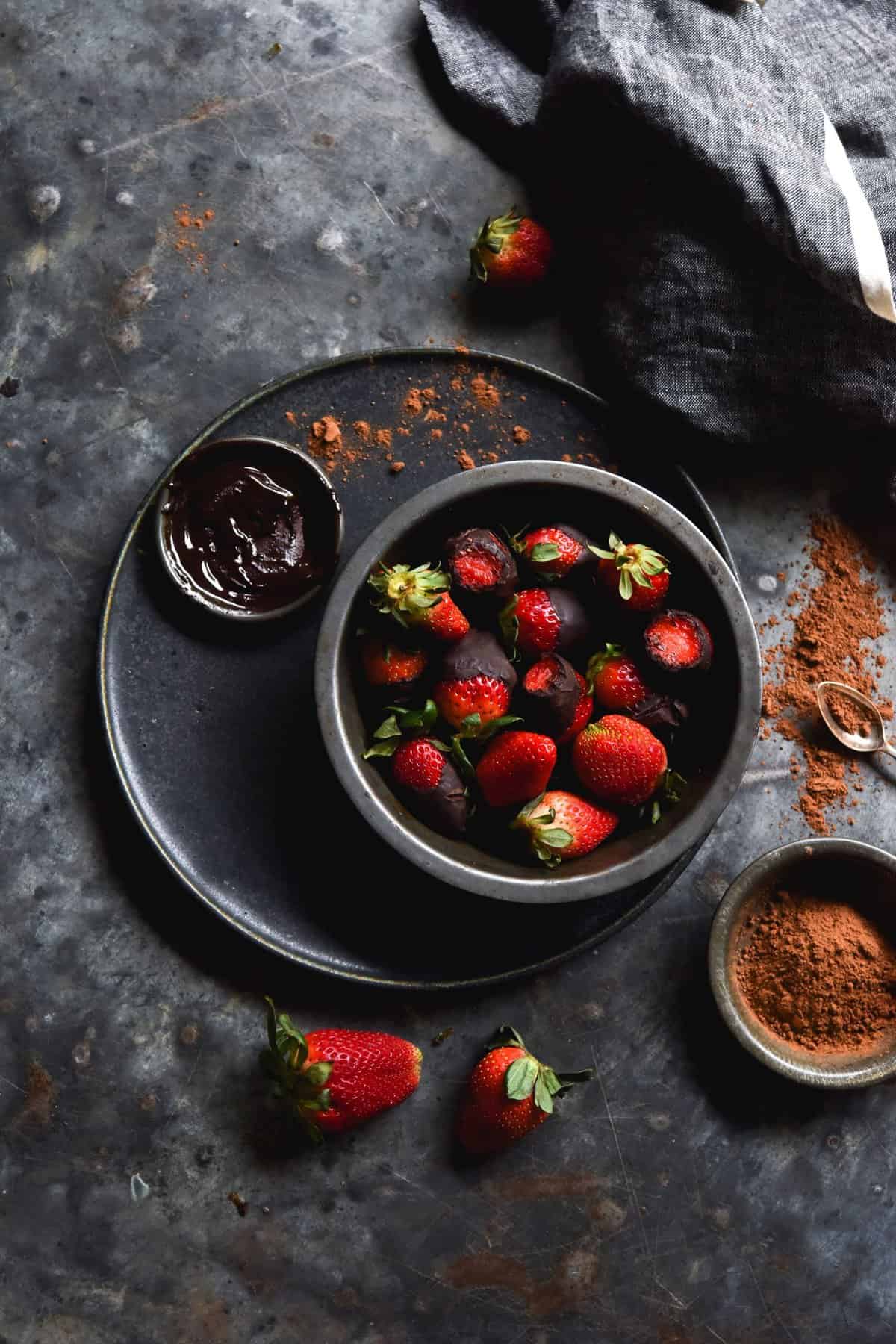 An aerial moody image of vegan chocolate covered strawberries on a dark backdrop