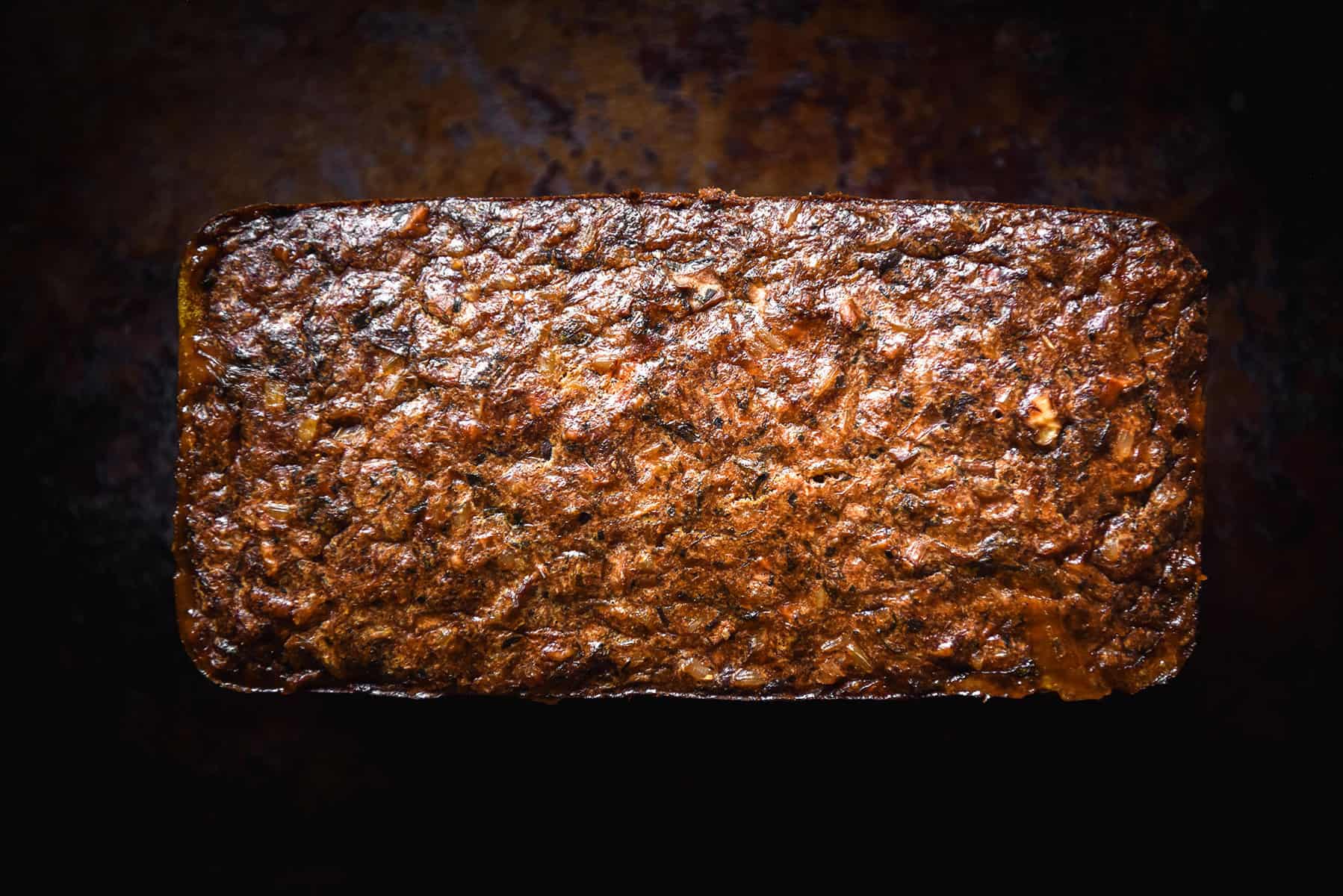 An aerial view of a golden brown FODMAP friendly vegetarian nut loaf. It sits atop a dark brown background