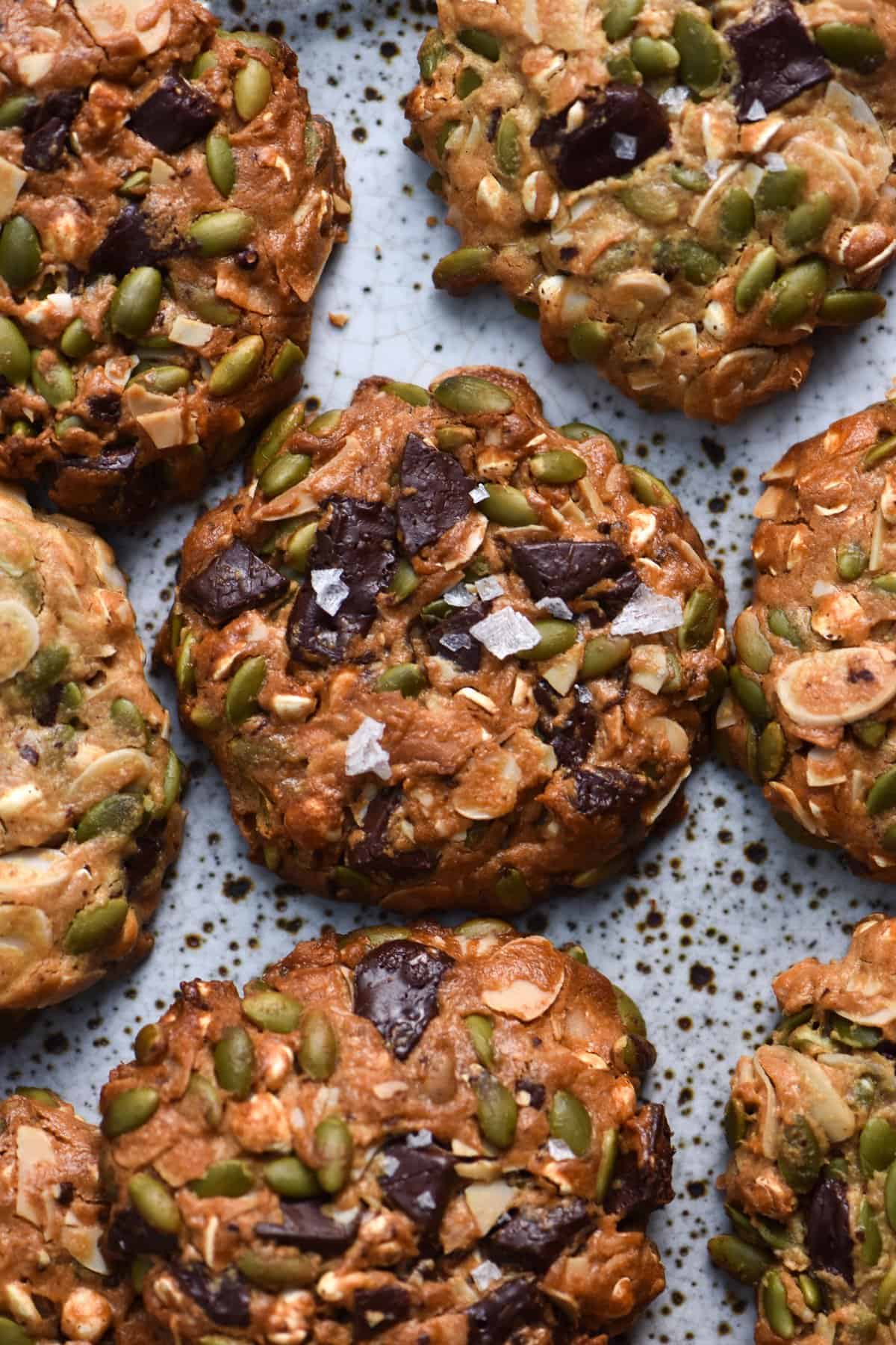 A close up of a plate of peanut butter nut and seed cookies with choc chips and sea salt flakes on top