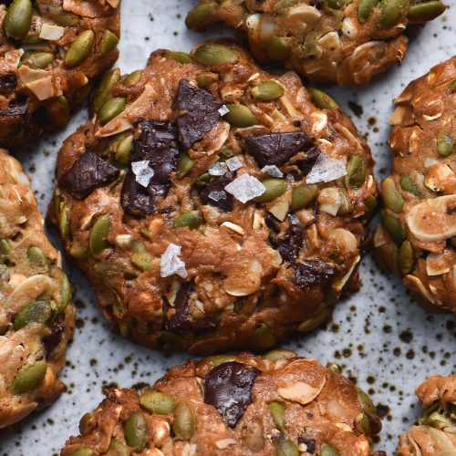 A close up of a plate of gluten free peanut butter cookies filled with seeds and topped with choc chips and sea salt flakes