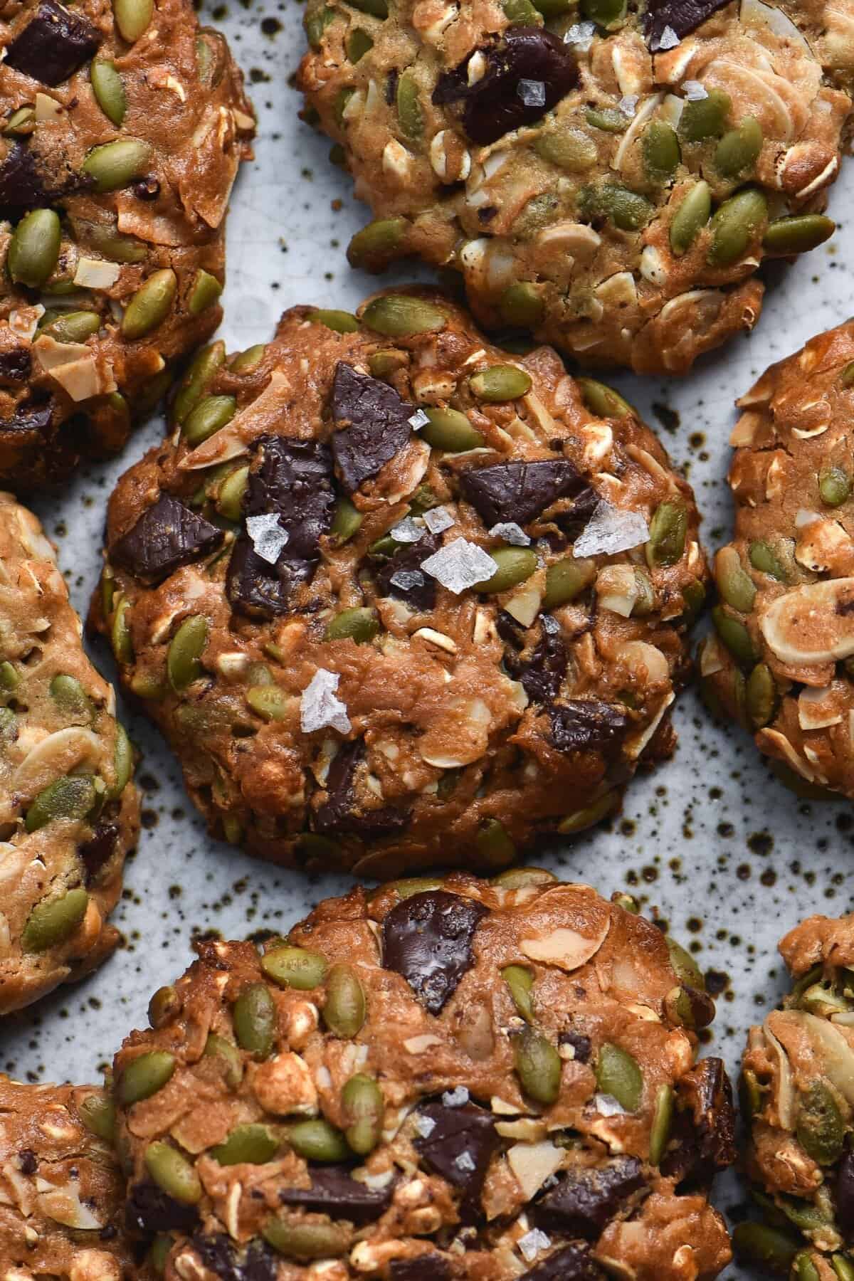 A close up of a plate of gluten free peanut butter cookies filled with seeds and topped with choc chips and sea salt flakes