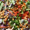 A close up shot of a Vegan Vietnamese coleslaw, topped with lots of toasted peanuts, spring onion greens and a wedge of lime,