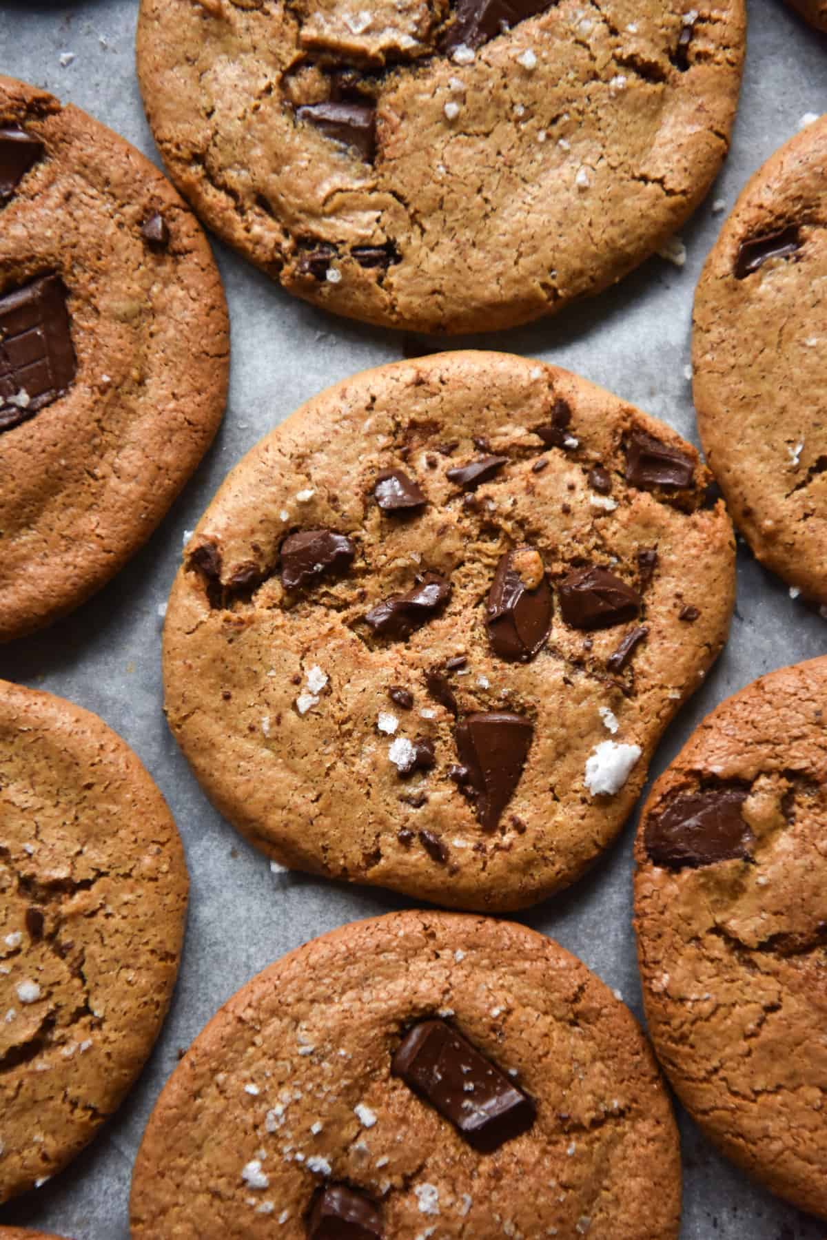 Vegan, gluten free choc chip almond butter cookies atop a baking tray lined with baking paper. Some of the cookies are sprinkled with sea salt flakes.