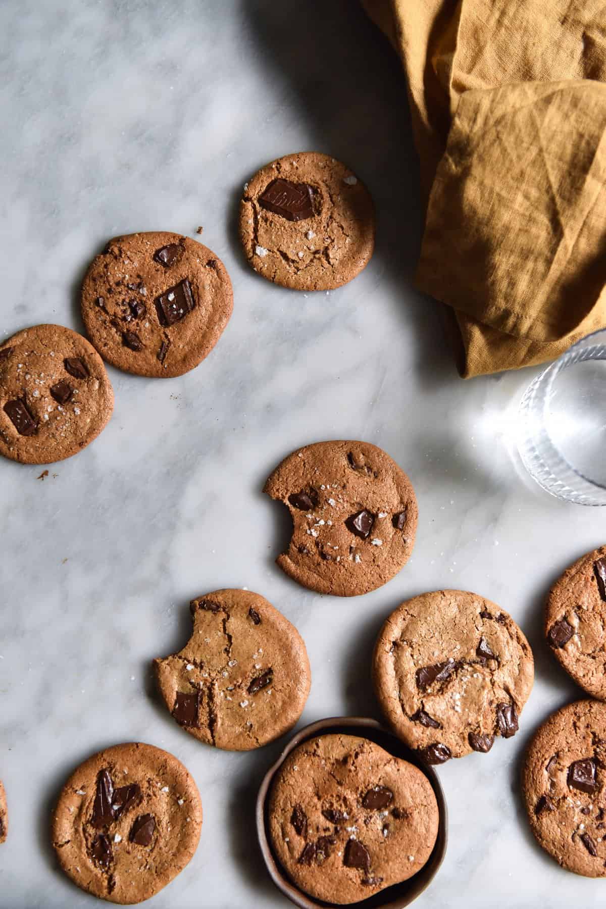 An aerial image of almond butter choc chip cookies casually arranged on a white marble table.