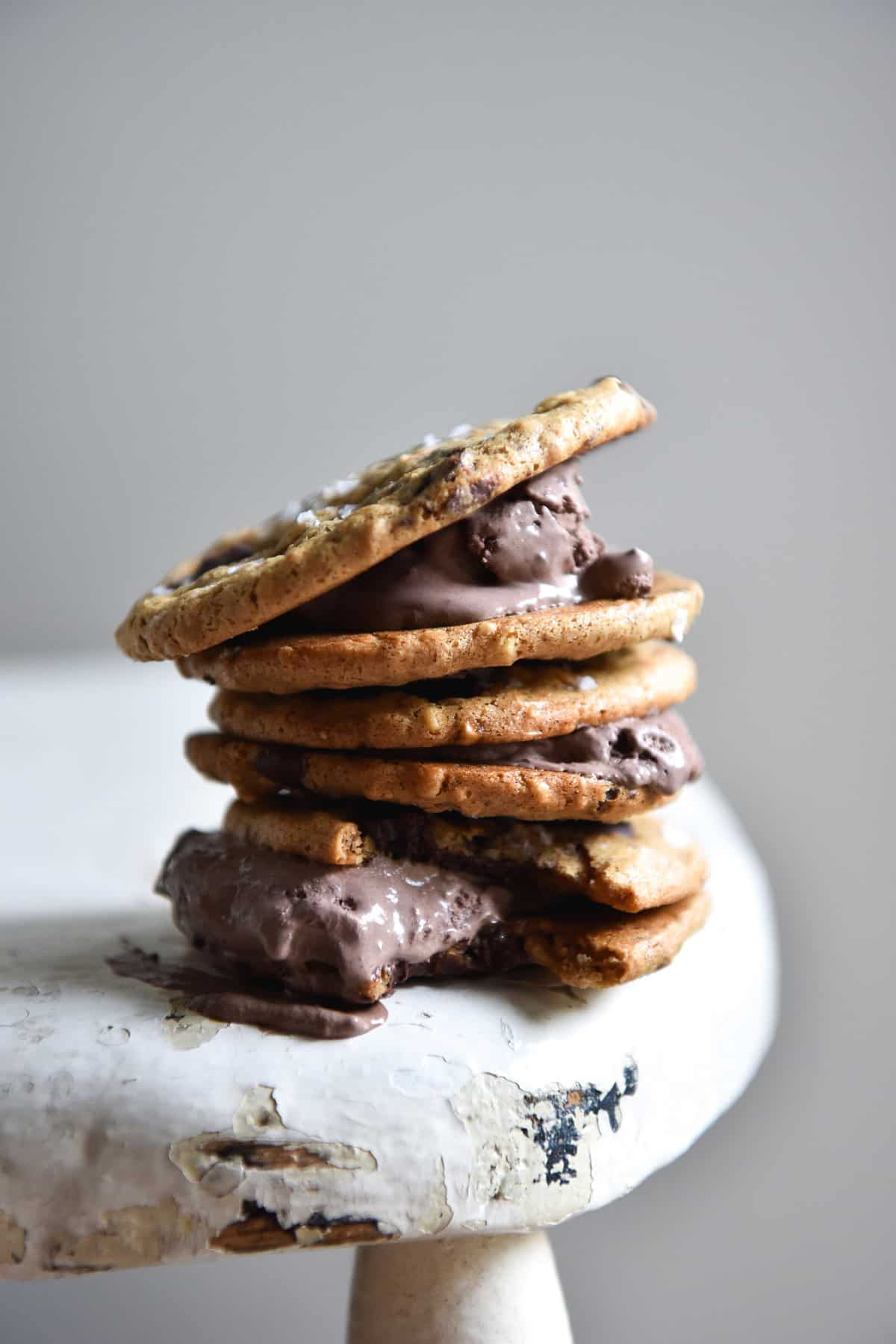 A side on image of peanut butter cookie ice cream sandwiches stacked on top of each other on a white vintage chair against a white backdrop