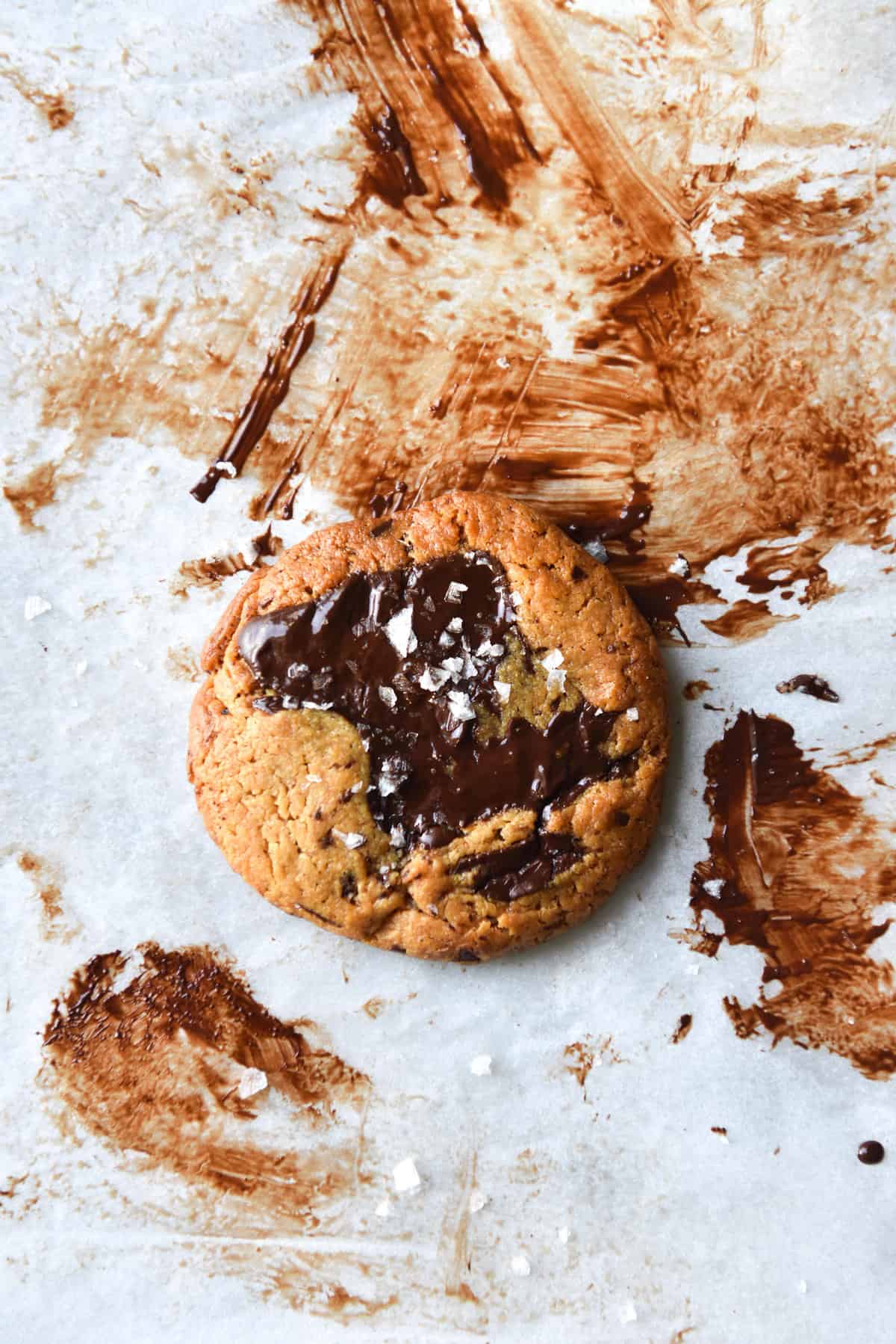 An aerial image of a gluten free peanut butter cookie on a sheet of baking paper that is covered in melted chocolate.