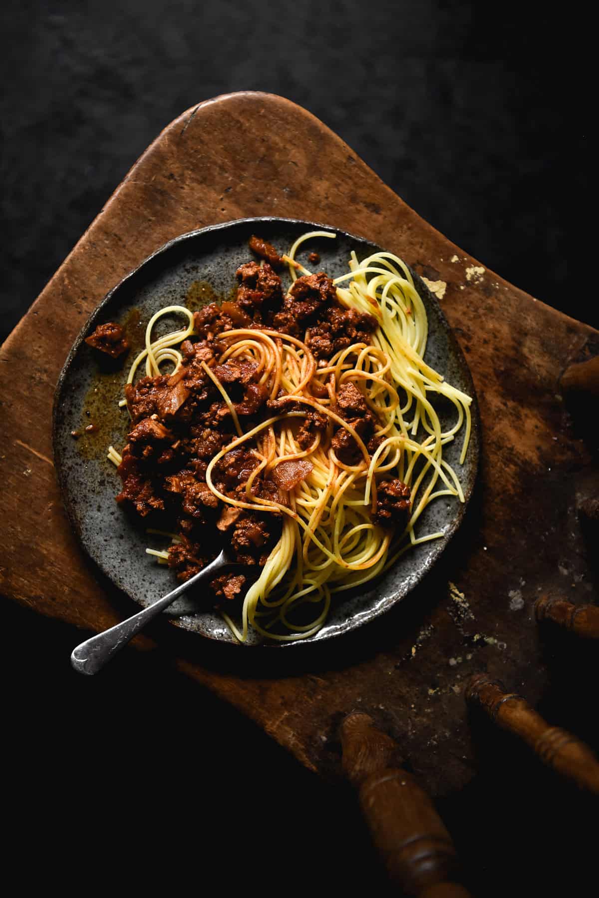 An aerial moody image of a plate of vegan bolognese on a wooden chair against a dark backdrop.