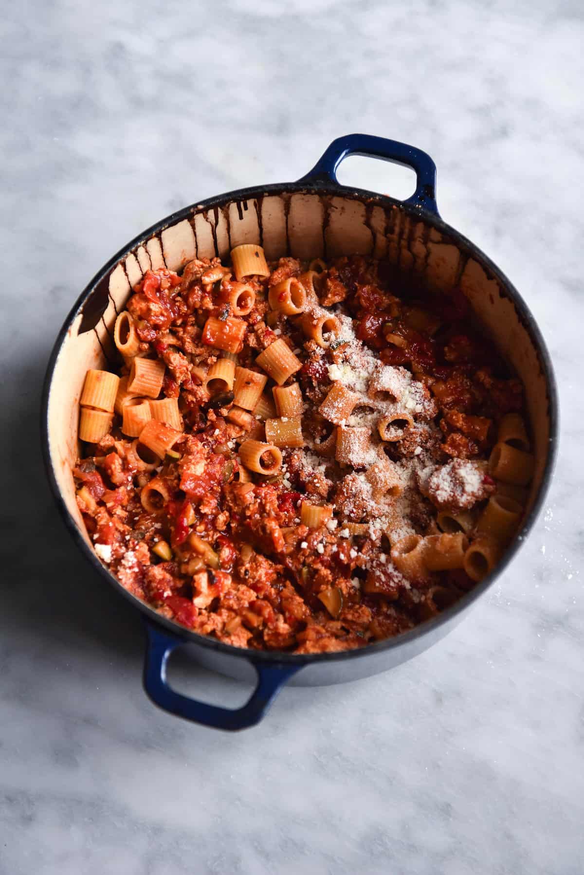 A pot of gluten free vegan bolognese pasta sits atop a white marble table