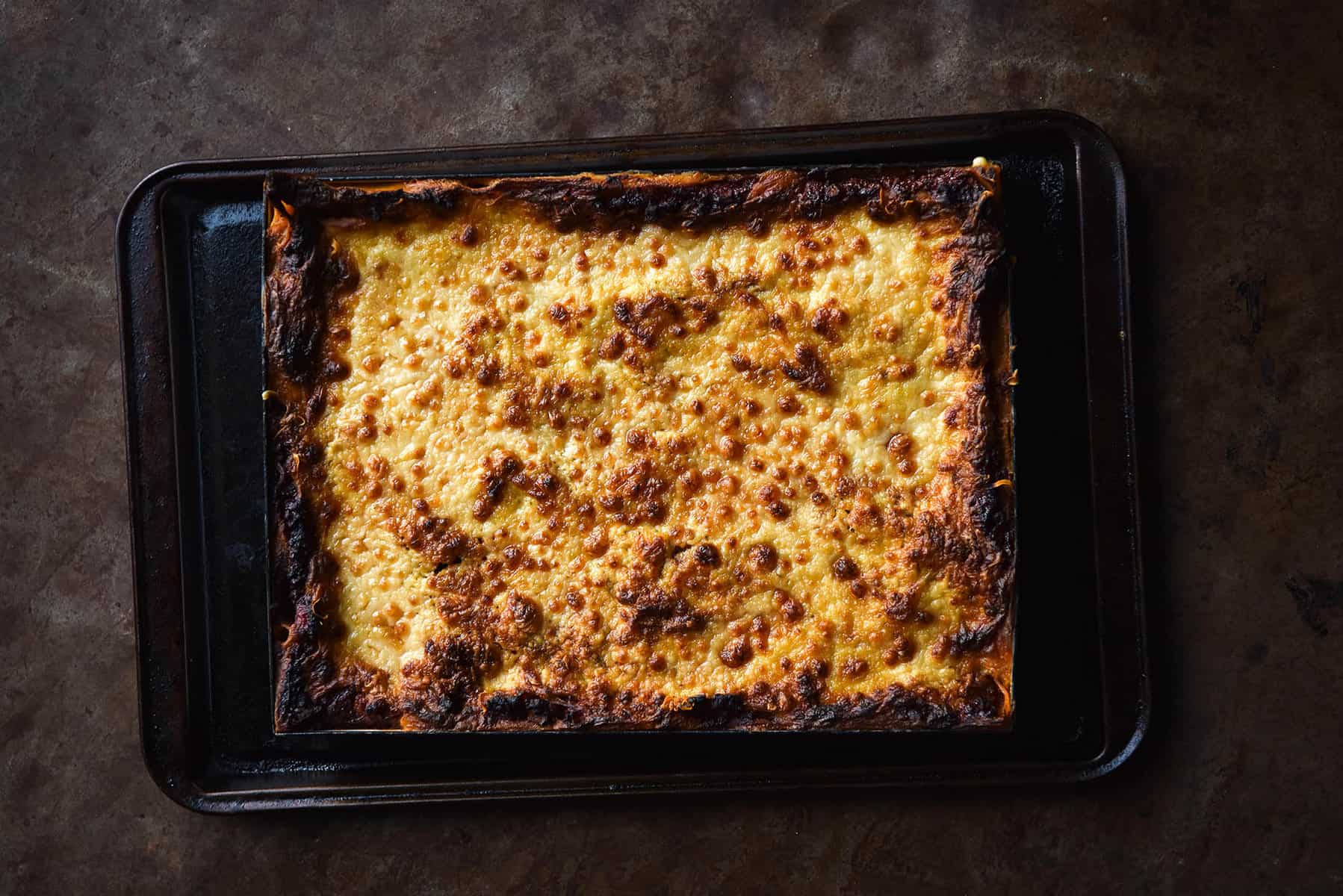 Vegan and gluten free lasagne covered in melty vegan cheese against a dark backdrop