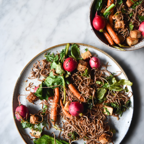 Sweet and sticky buckwheat noodles with crispy tofu and vegetables on a white marble table