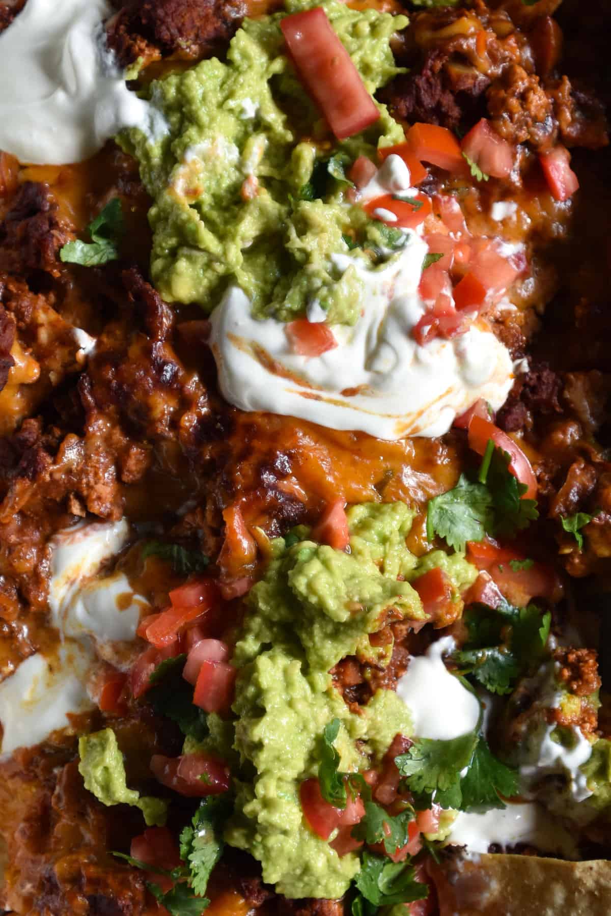 An aerial macro close up of a tray of low FODMAP vegetarian nachos. The nachos are topped with sour cream, avocado and a tomato coriander salsa.