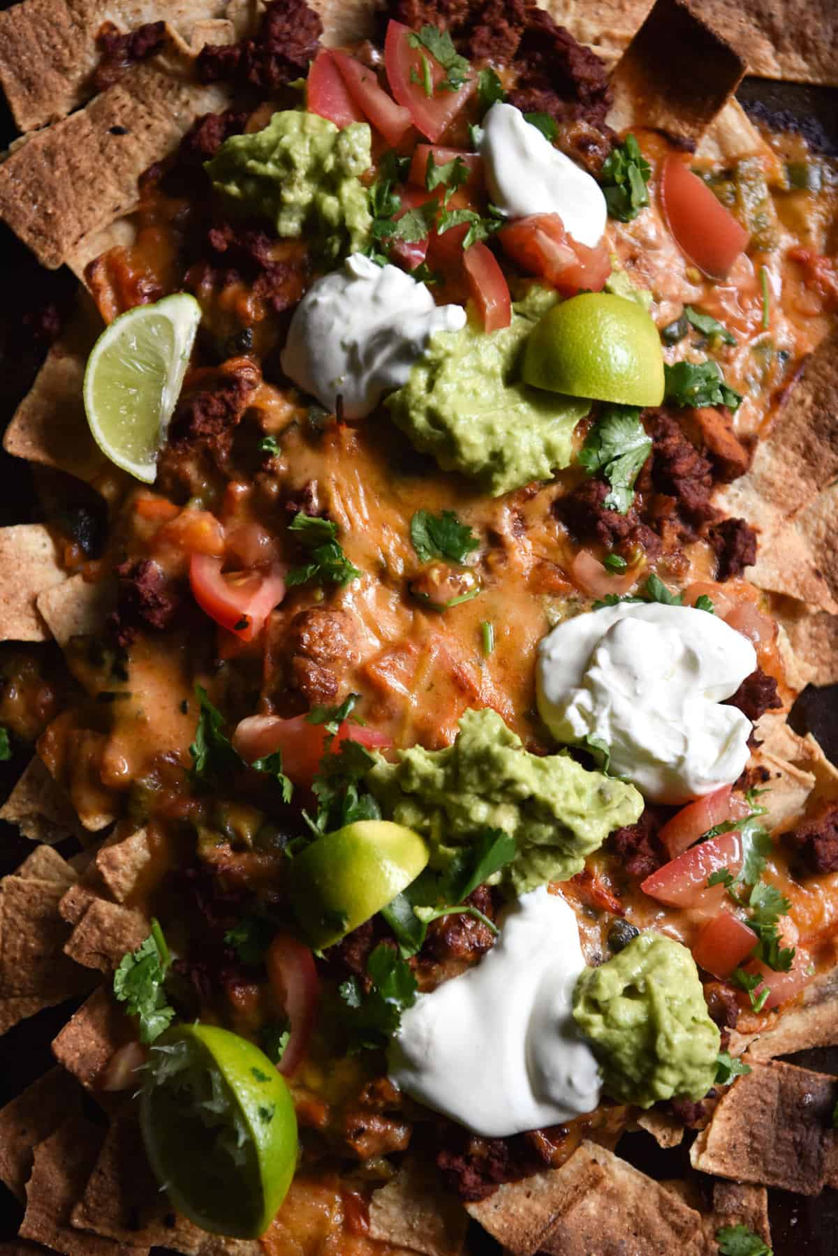 An aerial close up of vegetarian nachos with 'mince' queso, guacamole and salsa. 