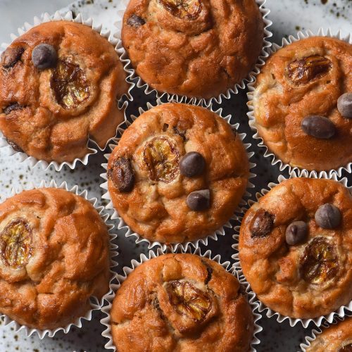 An aerial image of gluten free banana muffins on a white speckled ceramic plate atop a white marble table.