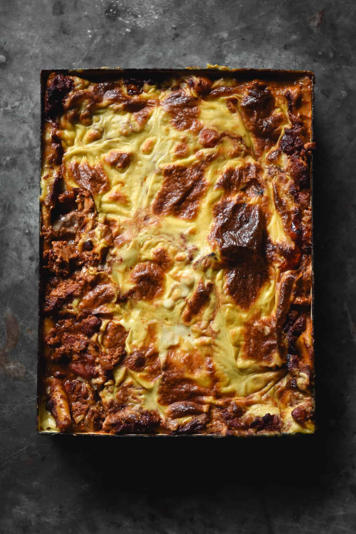 An aerial view of a gluten free, FODMAP friendly and vegan 'mince' lasagne on a dark steel backdrop