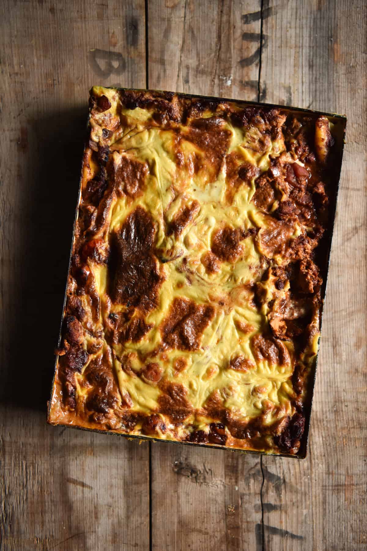 An aerial image of a FODMAP friendly vegan lasagne in a white rectangular baking dish. The lasagne sits atop a medium wood backdrop