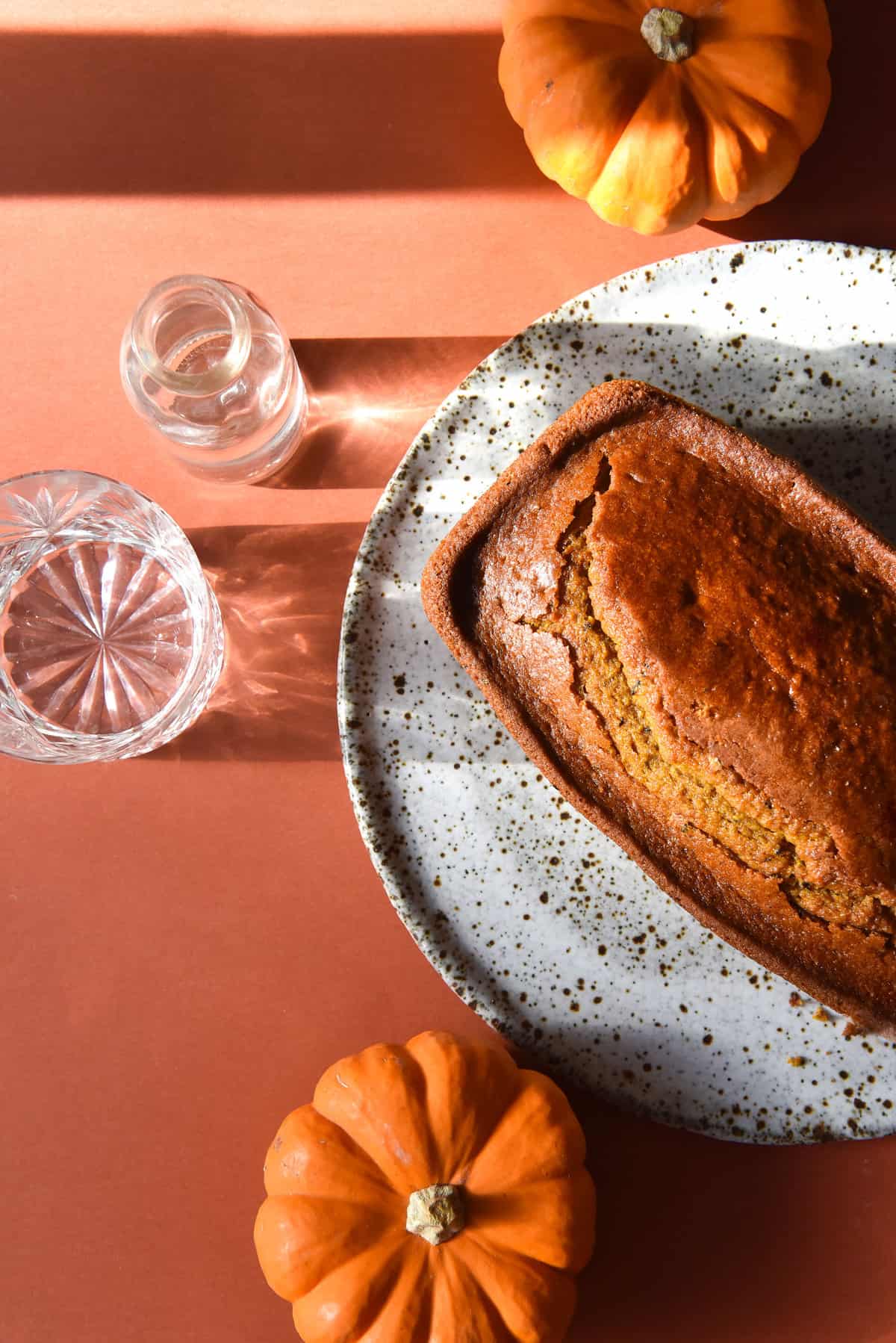 Gluten free pumpkin loaf on a white ceramic plate atop an orange backdrop